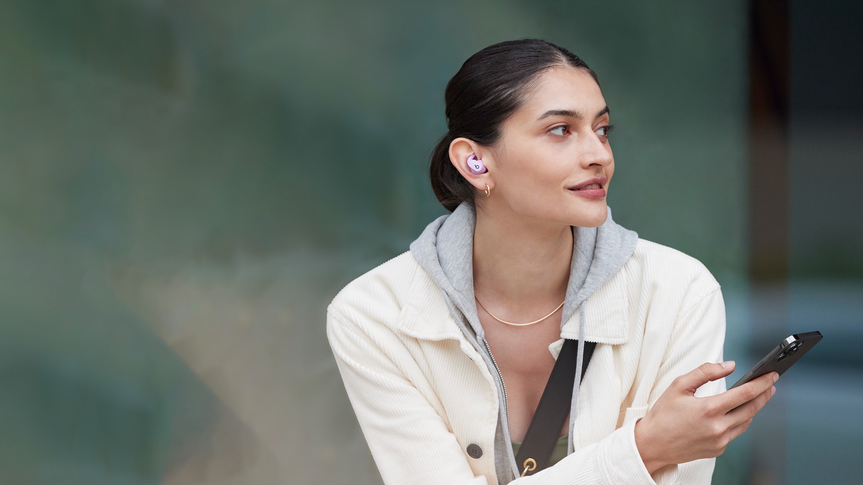 Woman wearing Beats Fit Pro and holding an iPhone outdoors