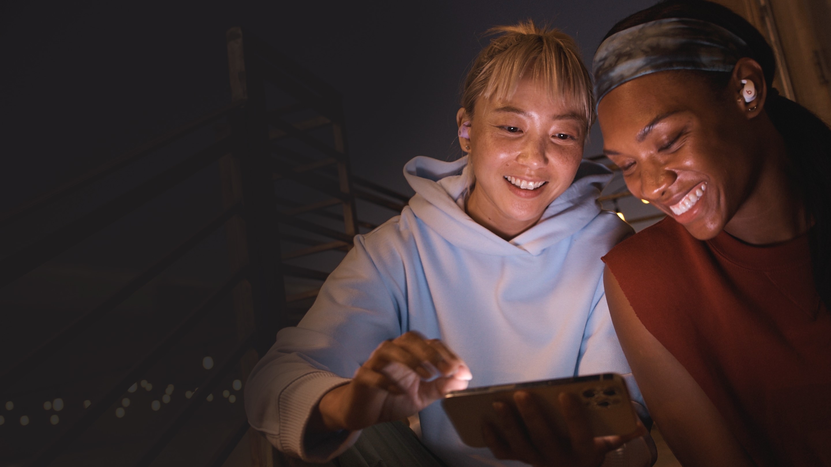 Two women wearing Beats Fit Pro and viewing an iPhone together